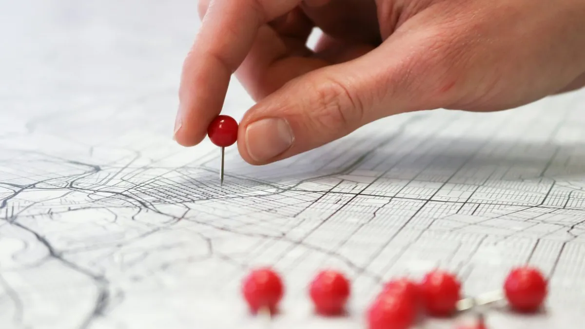 Hand placing a red pin on a city map