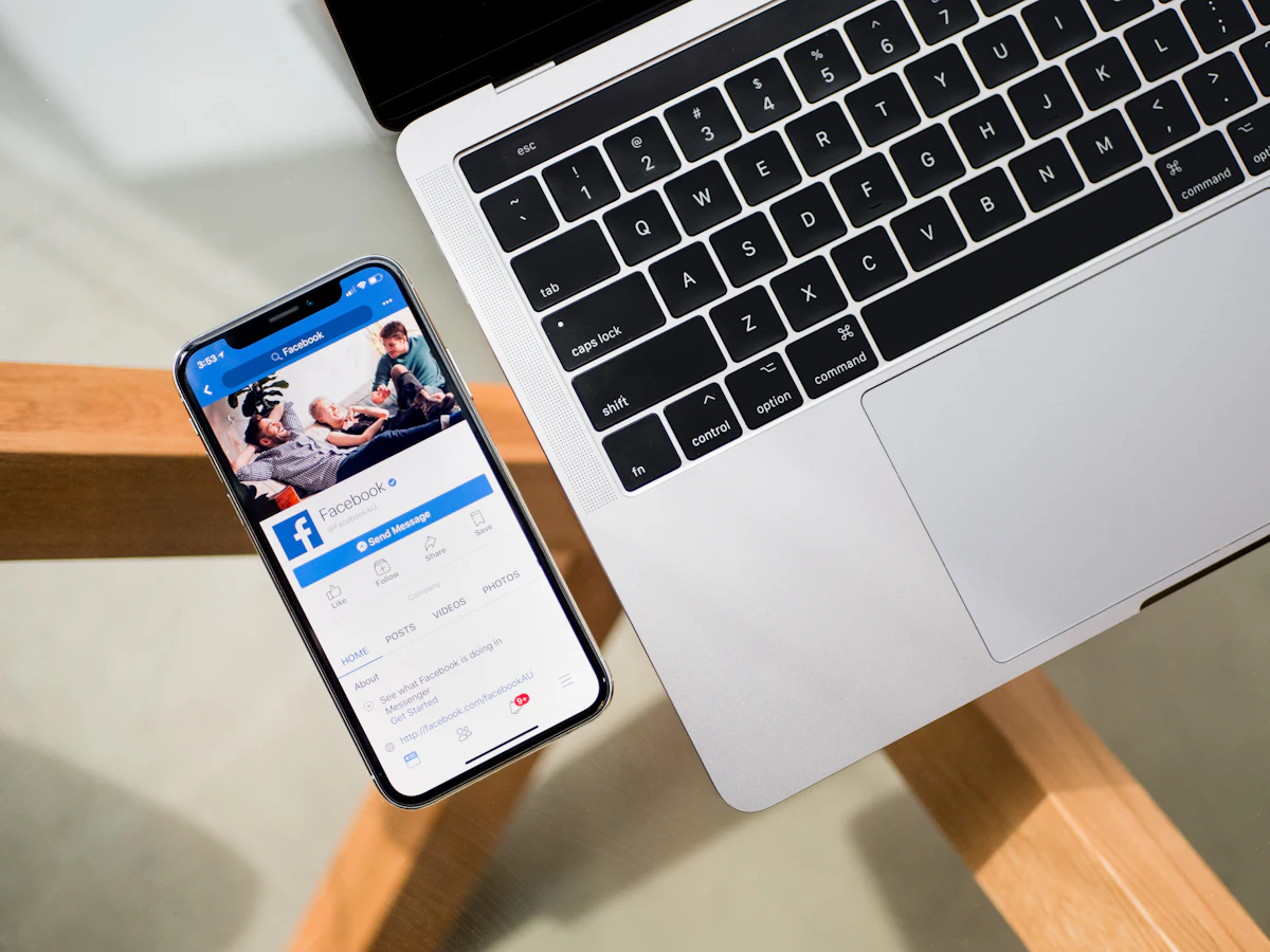 Smartphone showing a Facebook page next to a laptop